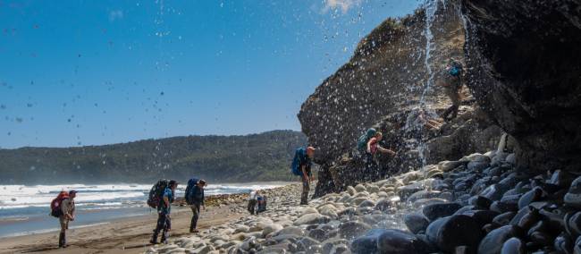 Trekking behind a waterfall on the South Coast Track | John Dalton